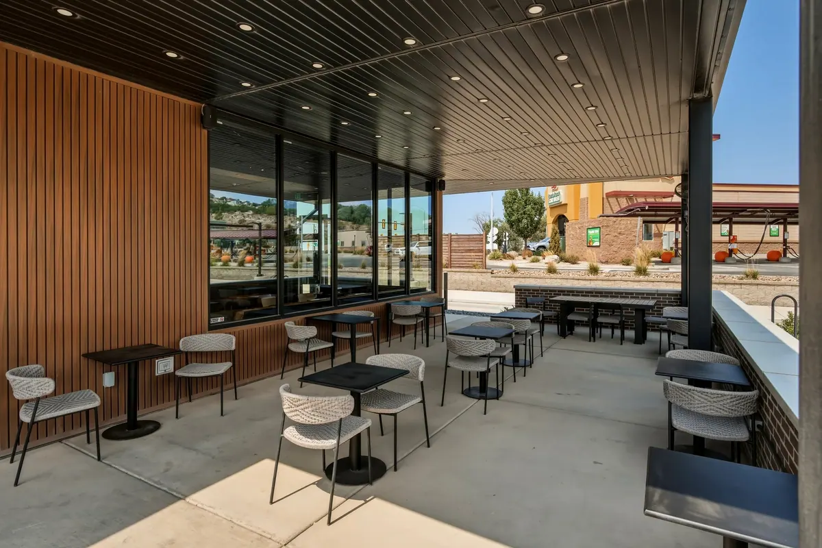 Covered outdoor seating area with wood accent wall, black ceiling and tables beside the Starbucks storefront.