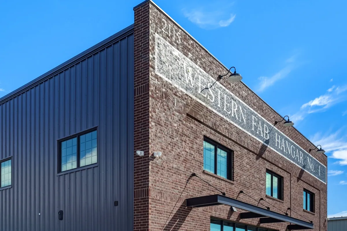 Close-up of the Western Fab hangar facade with brickwork, metal siding and upper windows