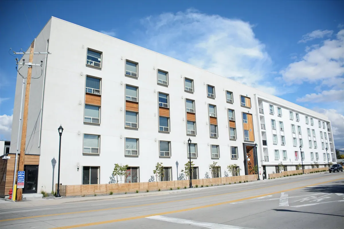 Long mid-rise multifamily building with white stucco and warm wood-toned accent panels designed by RAD Architectural Design