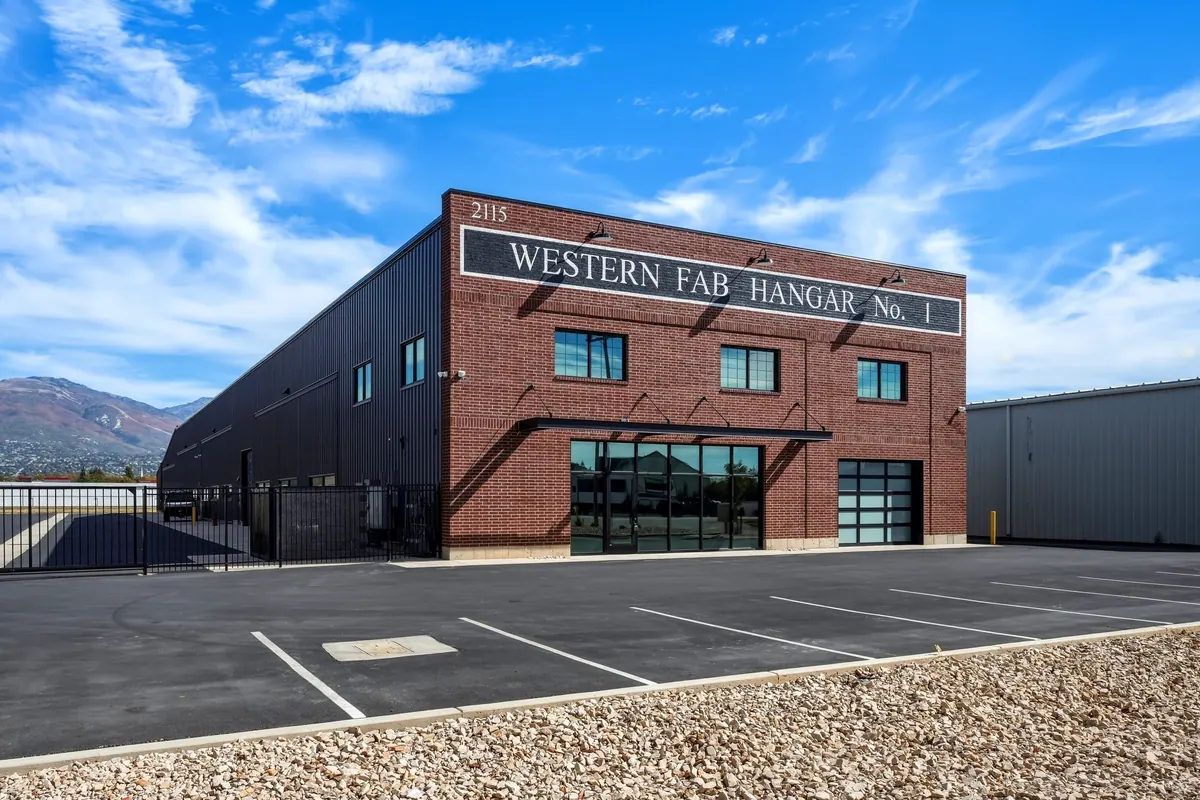 Ground-level exterior of a Western Fab airplane hangar showing the brick entrance facade and adjacent metal-sided hangar